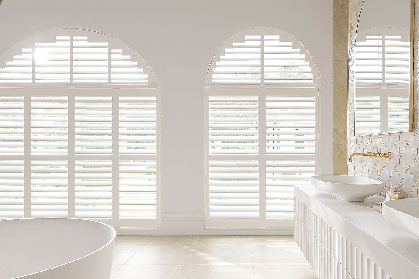 polysatin-shutters-benefit-06 Classic transitional style white bathroom with large radius windows covered by Polysatin Shutters, offering light and privacy control in the bathroom. Suitable for wet areas. For sale in our Brisbane showroom.