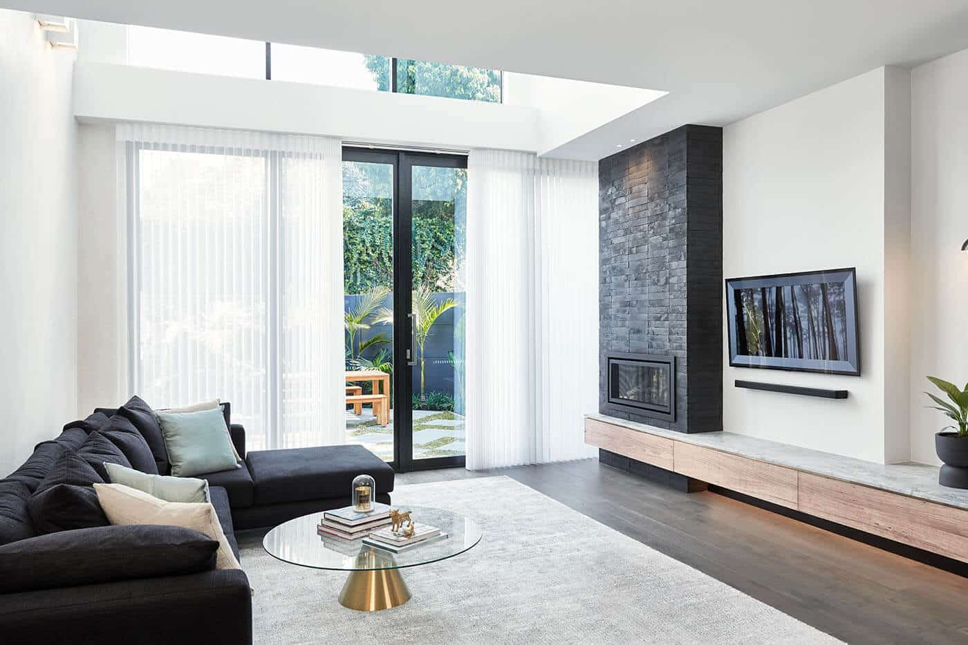 Minimal living room design with white walls, black chimney and couch in Brisbane featuring Luminette Privacy Sheers covering a large window showing the outside house garden.