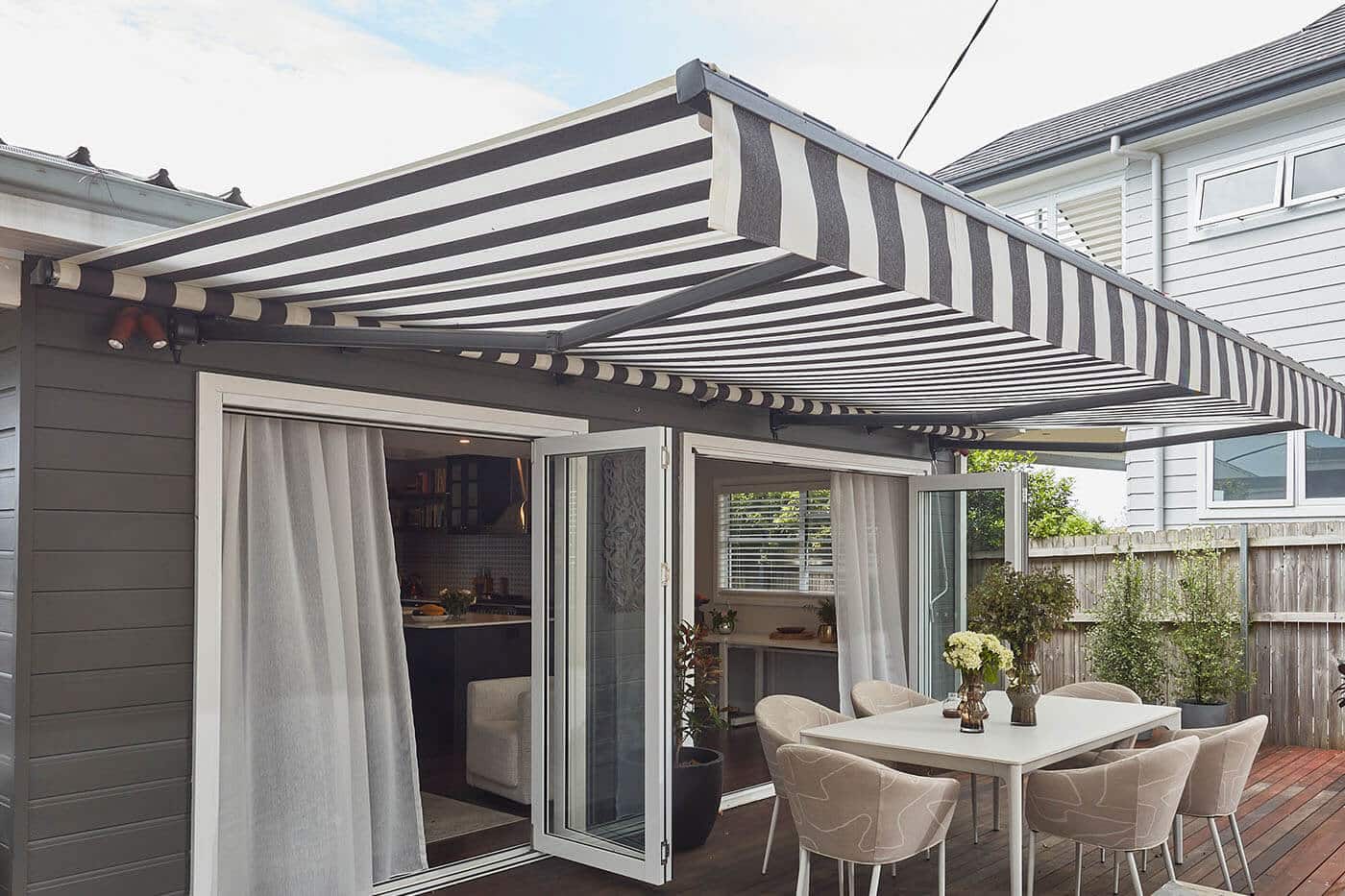 folding-arm-awning-benefit-02 Patio of mid-century home style with dinning table, covered by a Motorised Folding Arm Awning. It can be retracted too. Made in Australia.