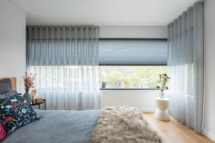 Modern transitional style blue-themed bedroom featuring long horizontal window panes partially covered by layers of curtain and sheers, giving the room a cozy and aesthetic look. On display in Complete Blinds Brisbane.