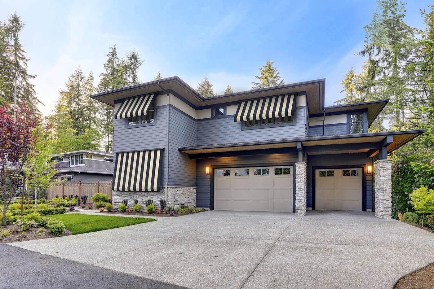 system-2000-awnings-benefits-02 Outside view of a blue mid-century style home with a garage, surrounded by trees, featuring Re-covering Awnings. Available in various styles and durable fabrics.
