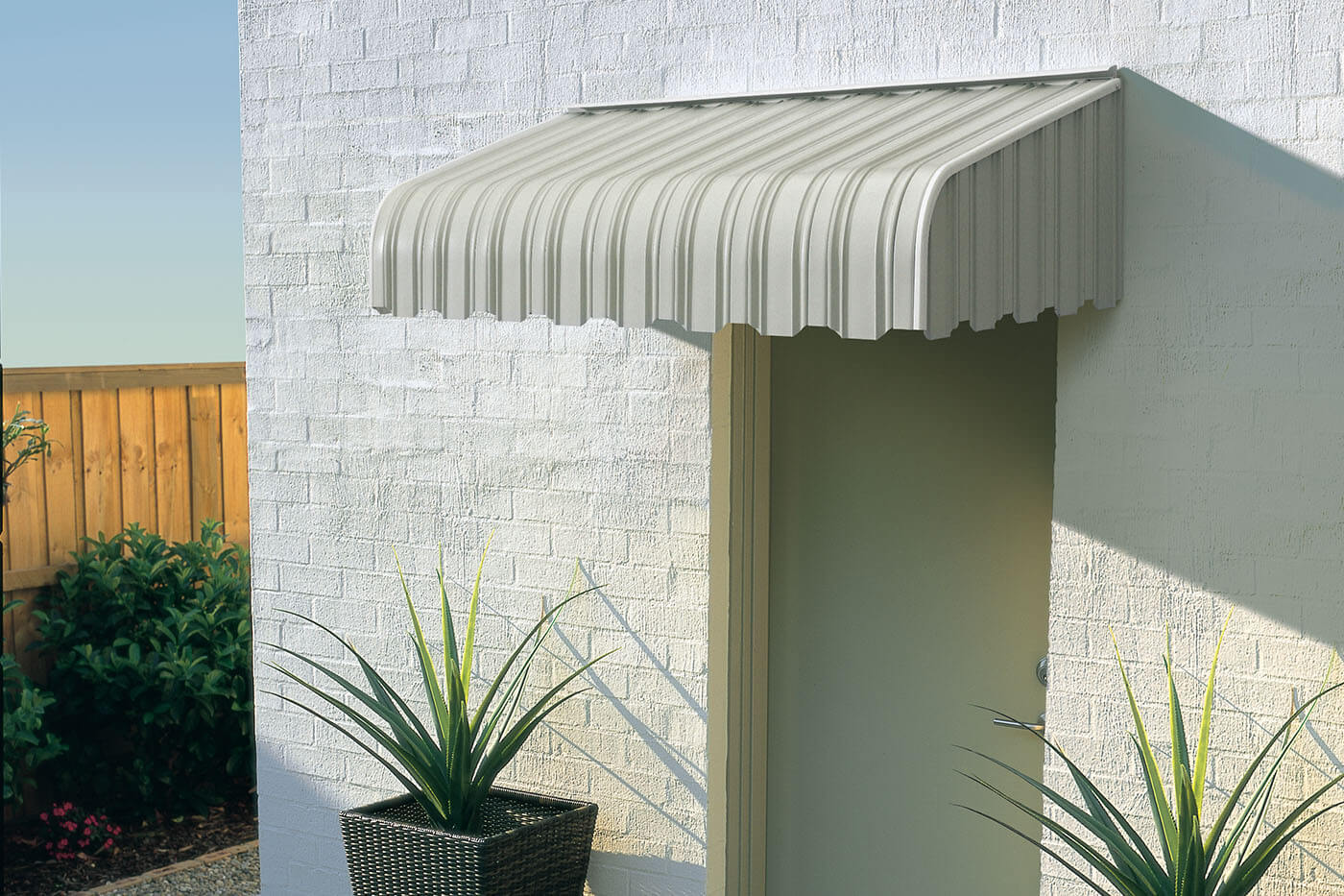 fixed-metal-awning-benefit-01 Outside view of a transitional-styled home with plants by the door, featuring Aluminium Awnings. Durable and perfect for shading. Available in Complete Blinds Australia.
