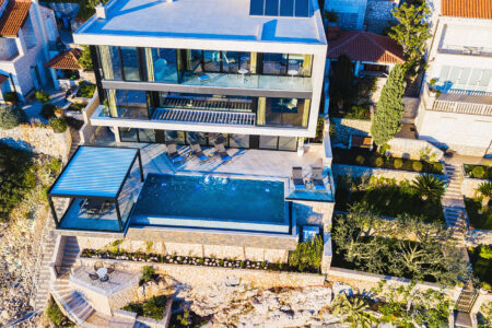 A bird's eye view of a luxurious triple storey home with swimming pool by the beach featuring Retractable Louvre Roof Pergola Awnings by Complete Blinds Brisbane.