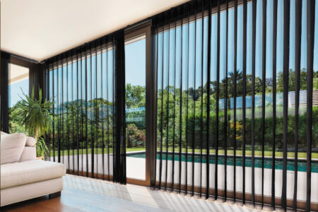 Modern and simple lounge area with wooden floors and ceiling-height windows covered with sheer black smart drapes, filtering sunlight into the room. Available at Complete Blinds Brisbane.