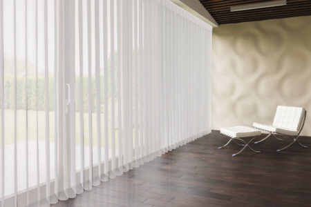 Contemporary minimalist lounge area with textured walls and wooden floors and ceiling-height windows covered with sheer white smart drapes, filtering sunlight into the room. Available at Complete Blinds Brisbane.