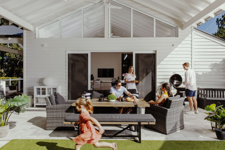 View of home with patio, family in the picture with a kid running around, featuring stacking door, installed by Complete Blinds Brisbane.