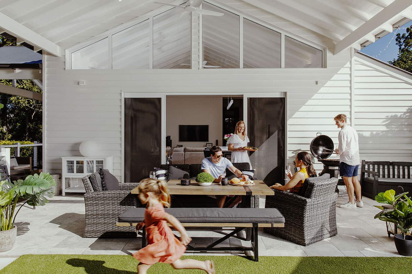 View of home with patio, family in the picture with a kid running around, featuring stacking door, installed by Complete Blinds Brisbane.
