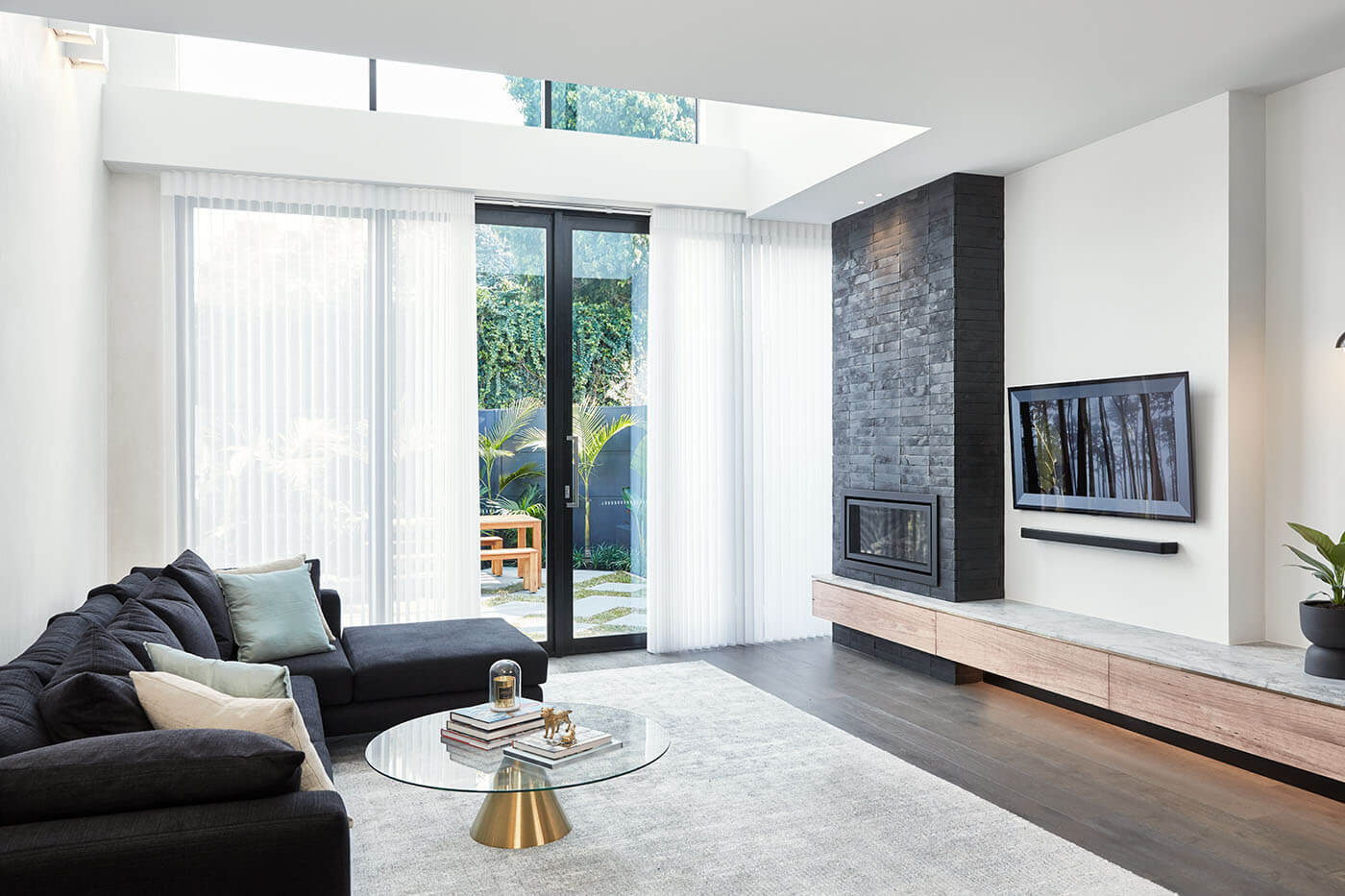 Minimal living room design with white walls, black chimney and couch in Chermside featuring Luminette Privacy Sheers covering a large window showing the outside house garden.