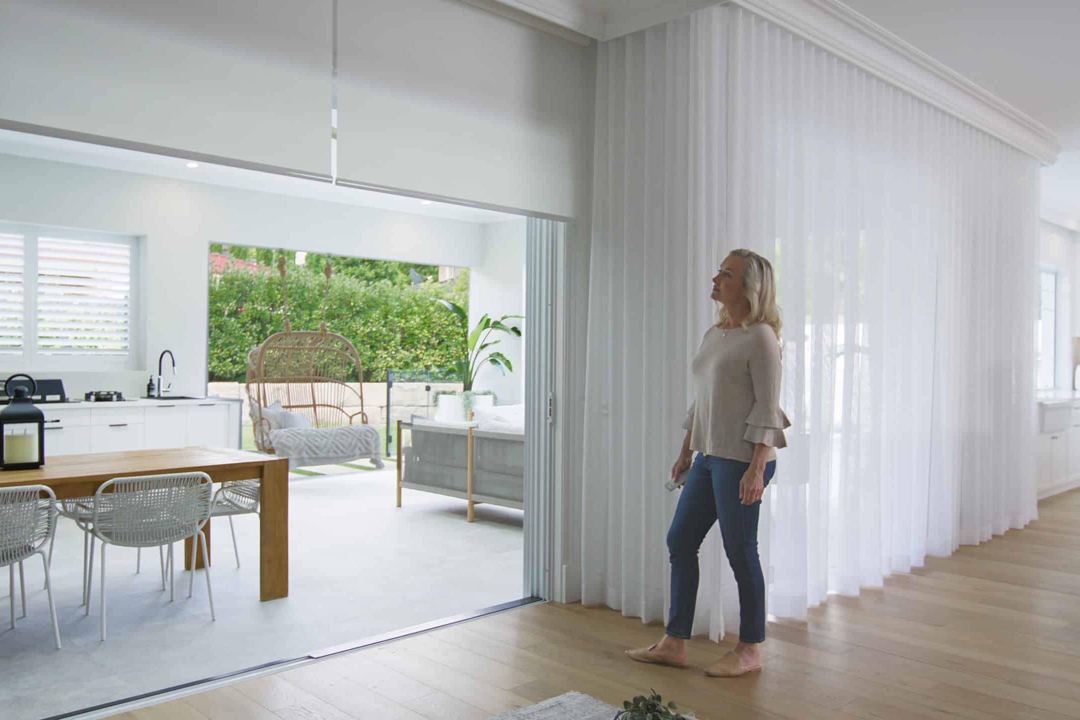 Complete_Blinds-11 Woman standing in an elegant and luxurious space, featuring sheer white curtains by Complete Blinds Queensland.